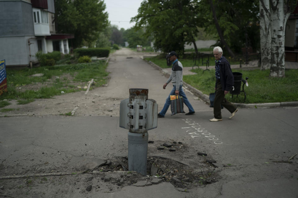 FILE - People walk past part of a rocket that sits wedged in the ground in Lysychansk, Luhansk region, Ukraine, Friday, May 13, 2022. War has been a catastrophe for Ukraine and a crisis for the globe. One year on, thousands of civilians are dead, and countless buildings have been destroyed. Hundreds of thousands of troops have been killed or wounded on each side. Beyond Ukraine’s borders, the invasion shattered European security, redrew nations’ relations with one another and frayed a tightly woven global economy. (AP Photo/Leo Correa, File)