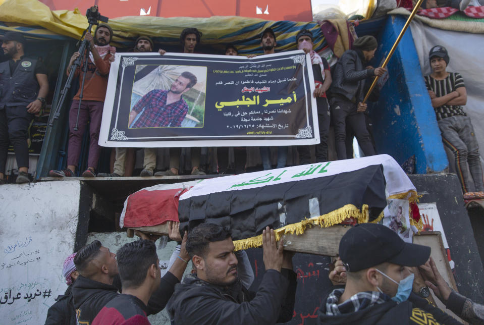 Mourners carry the body of their fellow protester Ameer al-Jalabib onto the top of cement blocks that separate them from riot police on a bridge, under a poster with his picture, his name and Arabic that reads "the hero Martyr," during his funeral in Tahrir Square, Baghdad, Iraq, Thursday, Dec. 26, 2019. Ameer succumbed to his wounds on Wednesday after being injured during anti-government demonstrations on October 27, 2019. (AP Photo/Nasser Nasser)