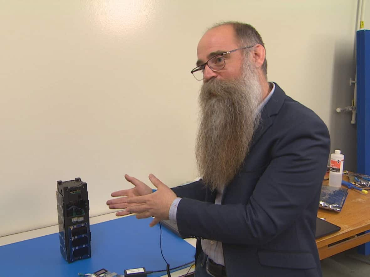 Philip Ferguson gestures towards Iris, the CubeSat satellite created by University of Manitoba engineering students. (Jeff Stapleton/CBC - image credit)