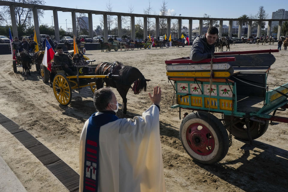 En la explanada del Santaurio Nacional de Maipú, un sacerdote bendice a creyentes que viajan en carretas tiradas por caballos durante una celebración en honor de la Virgen del Carmen, patrona de Chile, en Santiago, el sábado 16 de julio de 2022. (AP Foto/Esteban Felix)