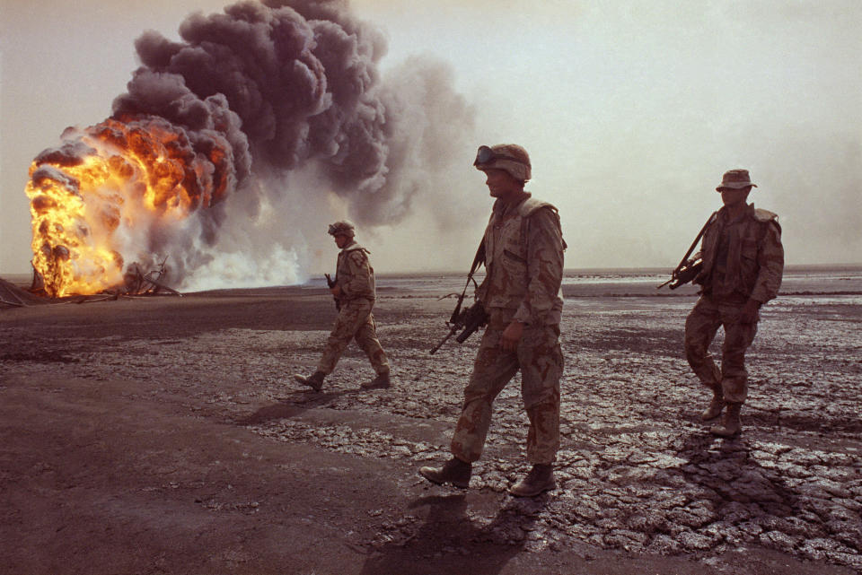 FILE - In this March 7, 1991 file photo, a U.S. Marine patrol walks across the charred oil landscape near a burning well during perimeter security patrol near Kuwait City. Former award-winning Associated Press photographer John Gaps III, who documented everything from war zones to the NCAA College World Series during his career, was found dead at his home Monday, Oct. 17, 2022, in Des Moines, Iowa, his family confirmed Tuesday. He was 63. (AP Photo/John Gaps III, File)