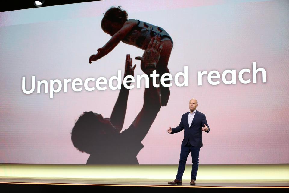 expedia group ceo peter kern stands in front of a large screen that says unprecedented reach with a man throwing a child in the air