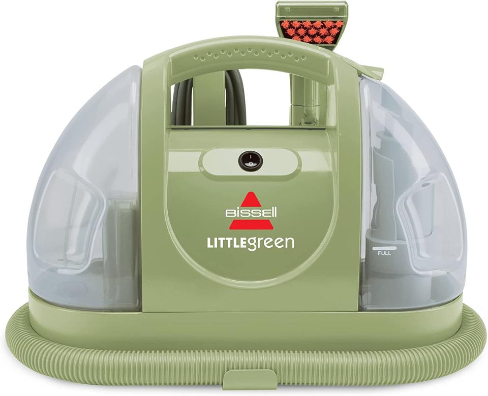 A Bissel Multi-Purpose Portable Carpet and Upholstery Cleaner in its green and transparent plastic case with attached brushes.