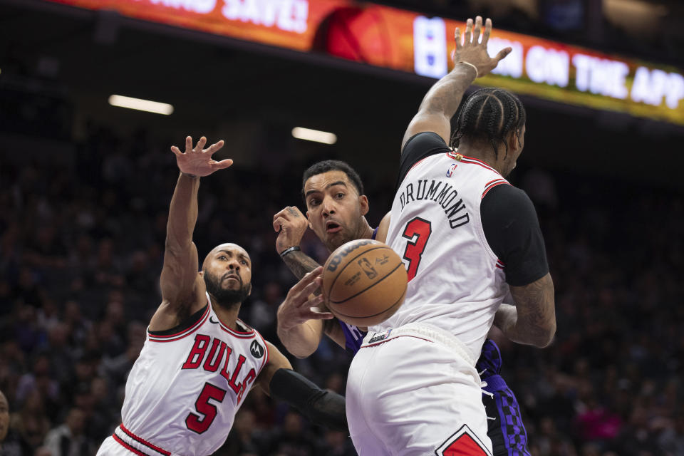 Sacramento Kings forward Trey Lyles, center, passes the ball between Chicago Bulls center Andre Drummond (3) and guard Jevon Carter (5) in the first quarter of an NBA basketball game in Sacramento, Calif., Monday, March 4, 2024. (AP Photo/José Luis Villegas)