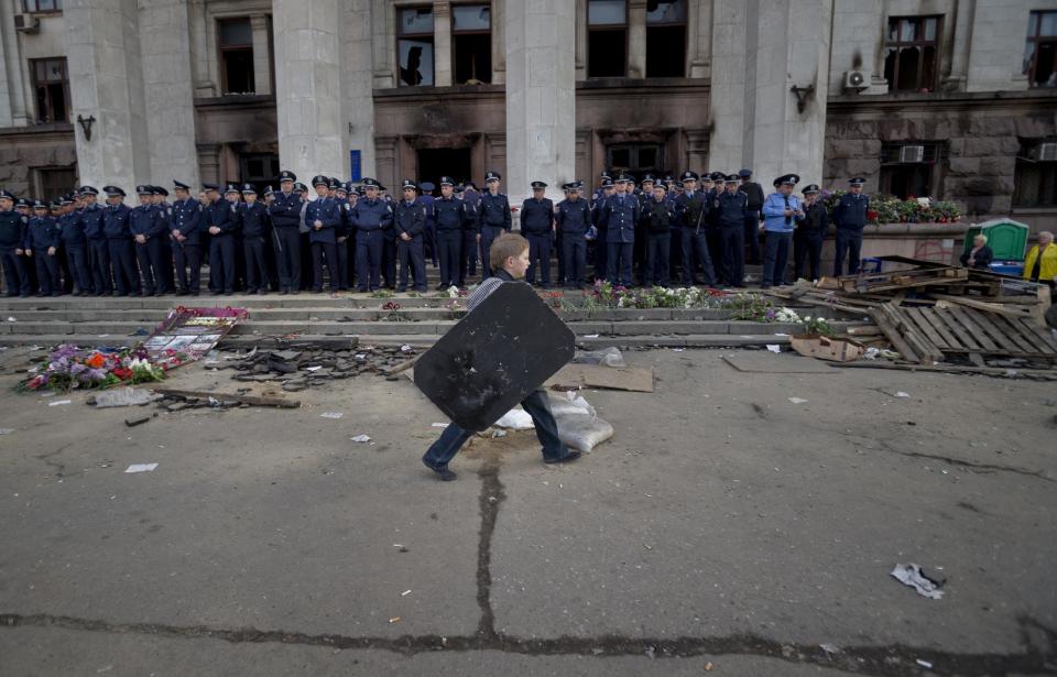 A child walks carrying a shield back dropped by police troops guarding the burnt trade union building in Odessa, Ukraine, Saturday, May 3, 2014, where more than 30 people died trying to escape during clashes the day before. Odessa had been largely tranquil since the February toppling of President Viktor Yanukovych, who fled to Russia. But clashes erupted Friday between pro-Russians and government supporters in the key port on the Black Sea coast, located 550 kilometers (330 miles) from the turmoil in the east. (AP Photo/Vadim Ghirda)