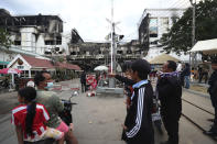Residents gather near a ruined building at the scene of a massive fire at a Cambodian hotel casino in Poipet, west of Phnom Penh, Cambodia, Friday, Dec. 30, 2022. The fire at the Grand Diamond City casino and hotel Thursday injured over 60 people and killed more than a dozen, a number that officials warned would rise after the search for bodies resumes Friday. (AP Photo/Heng Sinith)