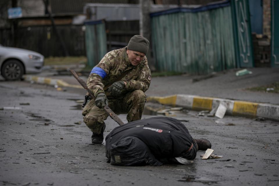 A Ukrainian serviceman uses a piece of wood to check if the body of a man dressed in civilian clothing is booby-trapped with explosive devices, in the formerly Russian-occupied Kyiv suburb of Bucha (Copyright 2022 The Associated Press. All rights reserved.)