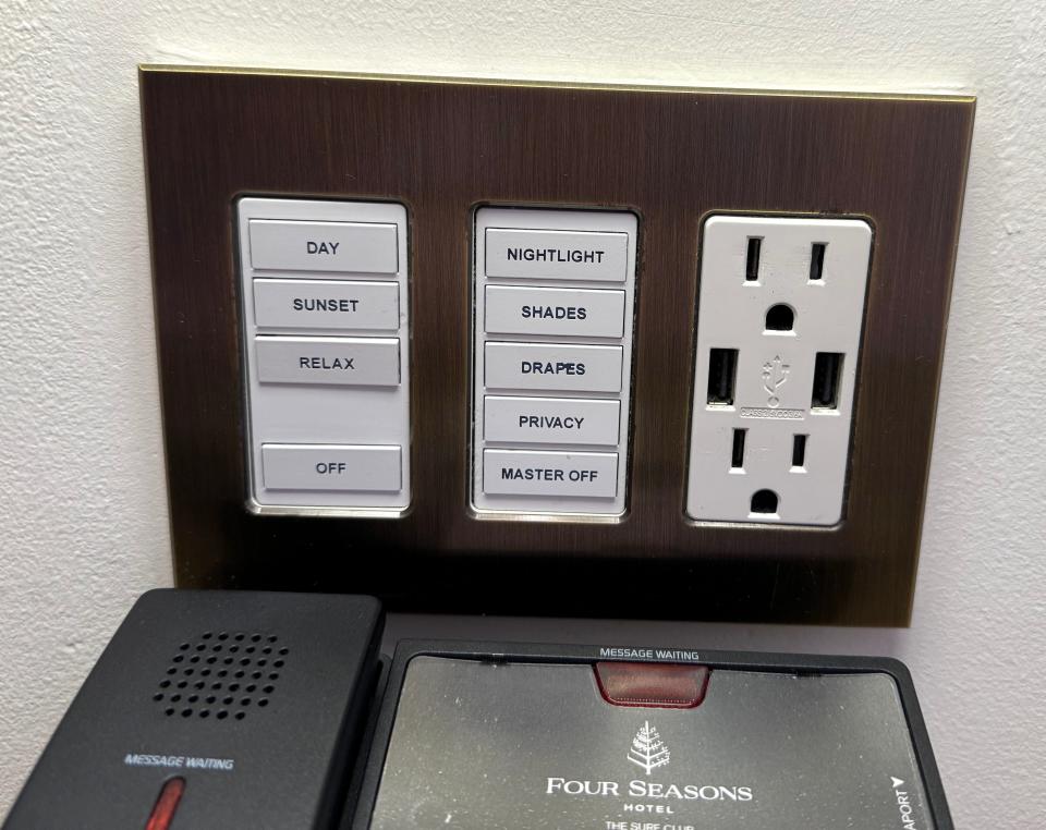 An outlet with controls for lighting and shades above a Four Seasons hotel phone.