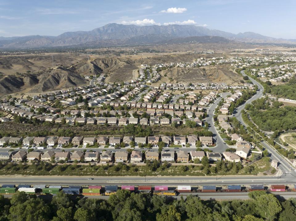 A train passing a housing development with mountains in the background