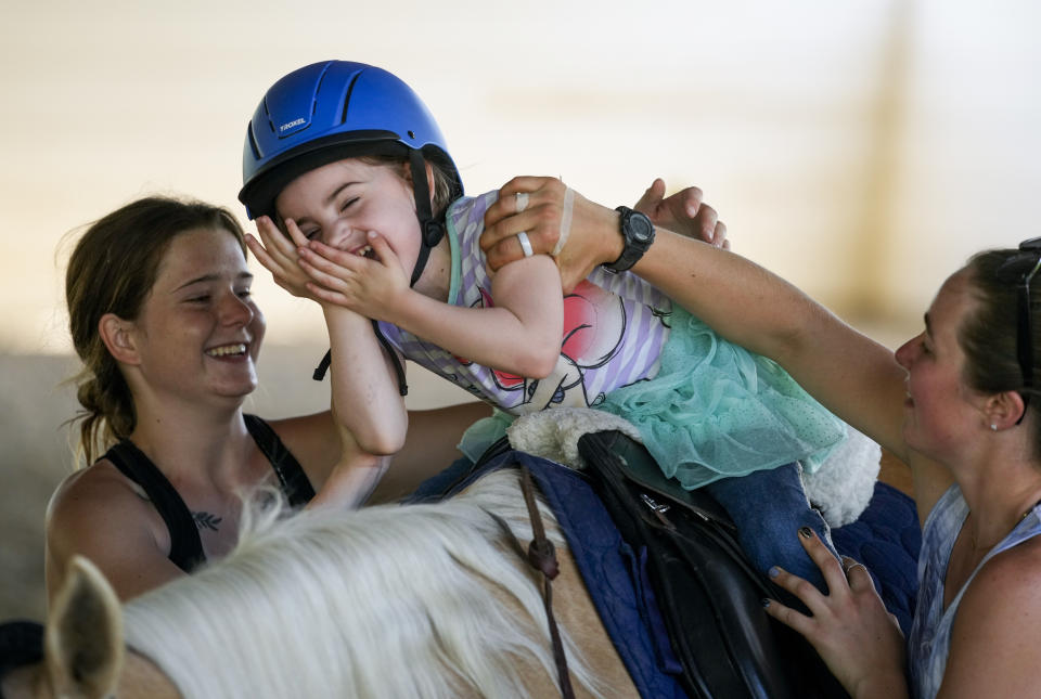 Jessi Hendrickson, a ranch attendant and instructor assistant, left, and riding instructor Atarah Brown, right, work with Scarlett Rasmussen, 8, as she laughs while riding horse Callie at the Foundation of Southern Oregon, May 17, 2023, in Rogue River, Ore. Chelsea Rasmussen fought for more than a year for her daughter, Scarlett, to attend full days at Parkside and says school employees told her the district lacked the staff to tend to Scarlett’s medical and educational needs, which the district denies. (AP Photo/Lindsey Wasson)