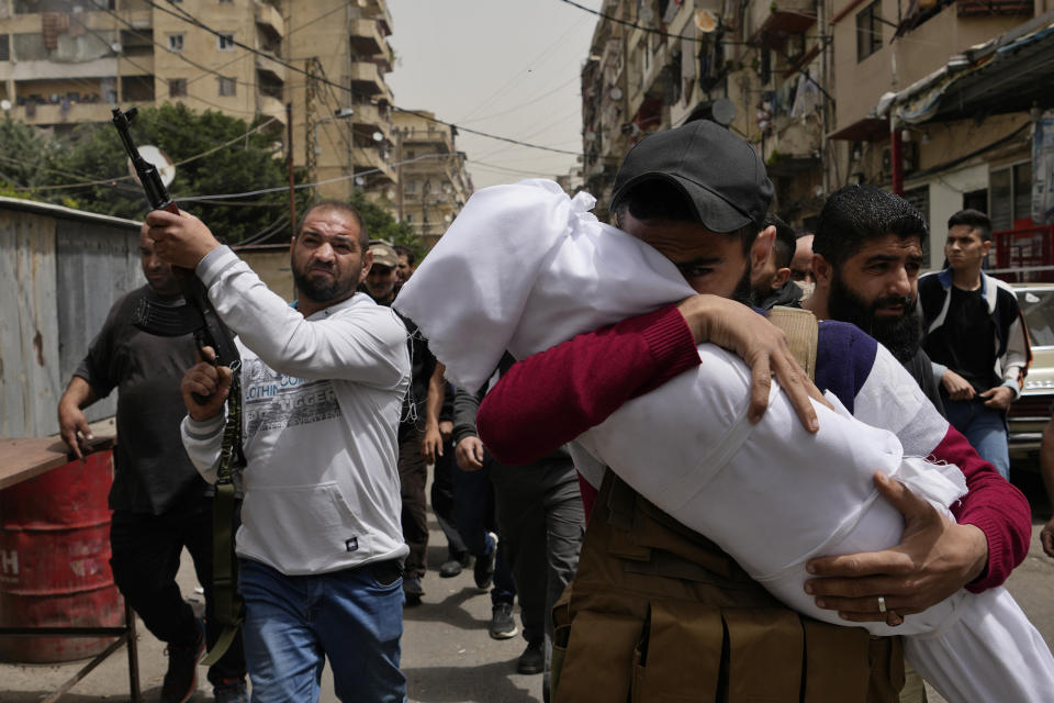 FILE - A man carries the body of a young girl, as a mourner fires in the air during the funeral procession for seven people killed when a boat packed with migrants sank over the weekend as the Lebanese navy tried to force it back to shore, in Tripoli, north Lebanon, Monday, April 25, 2022. A week ago, a boat carrying around 60 Lebanese trying to escape their country and reach Europe sank in the Mediterranean after colliding with a Navy ship. At least seven people are known dead and at least six are missing. The tragedy underscored the desperation among many Lebanese after the collapse of their country's economy.(AP Photo/Hassan Ammar, File)