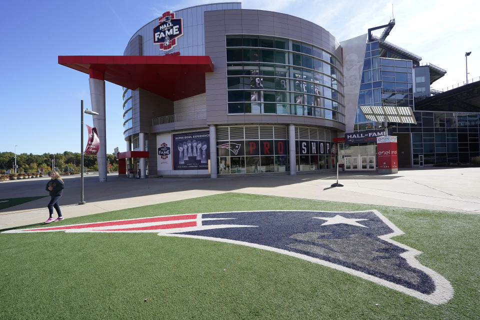 A passer-by walks past a New England Patriots football team logo near the Patriots ProShop at Gillette Stadium, Sunday, Oct. 11, 2020, in Foxborough, Mass. The NFL has postponed the Denver Broncos-New England Patriots game due to another positive coronavirus test with the Patriots. (AP Photo/Steven Senne)