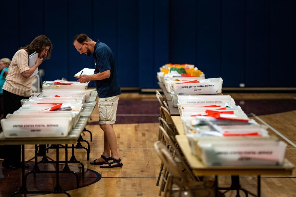 A person standing between tables with containers of election ballots