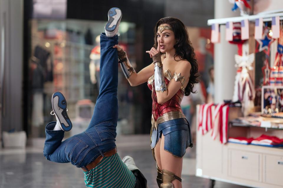 Wonder Woman poses with finger to lips while dangling a man upside down from one hand