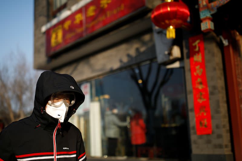 A man wearing a face mask and protective goggles walks along the street as the country is hit by an outbreak of the new coronavirus, in Beijing