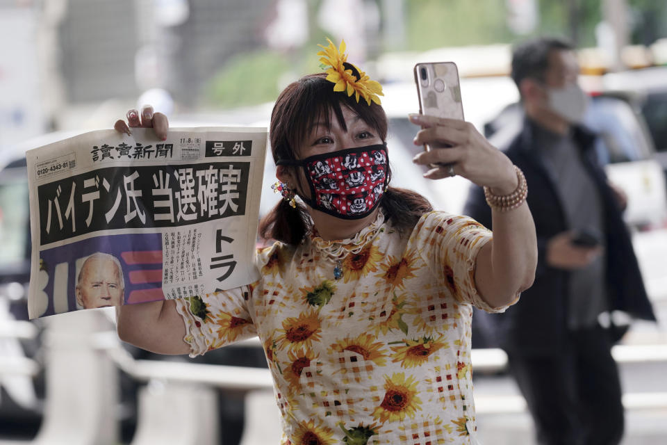 A passer-by takes a selfie with an extra newspaper reporting on President-elect Joe Biden's win in the U.S. presidential election, in Tokyo Sunday, Nov. 8, 2020. The headline reads: “Mr. Biden Assured to win.”(AP Photo/Eugene Hoshiko)