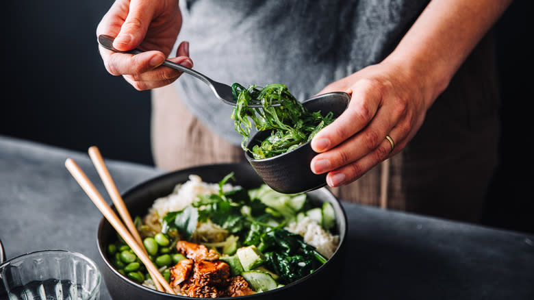 Hands adding seaweed to a stir fry