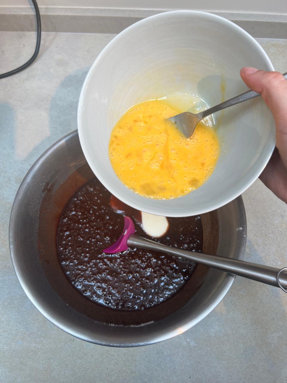A bowl of whisked eggs being held over the bowl of batter.