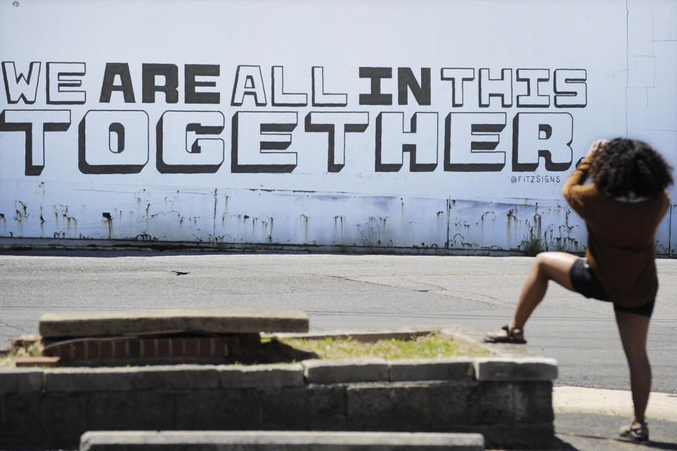 FILE - In this Thursday, April 16, 2020 file photo, a passerby photographs a message reading "WE ARE ALL IN THIS TOGETHER" painted on the side of a building in Homewood, Ala., during the cornovavirus outbreak. (AP Photo/Jay Reeves)