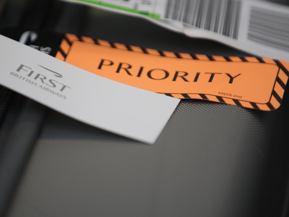 A British Airways priority baggage label and First Class label on a suitcase.