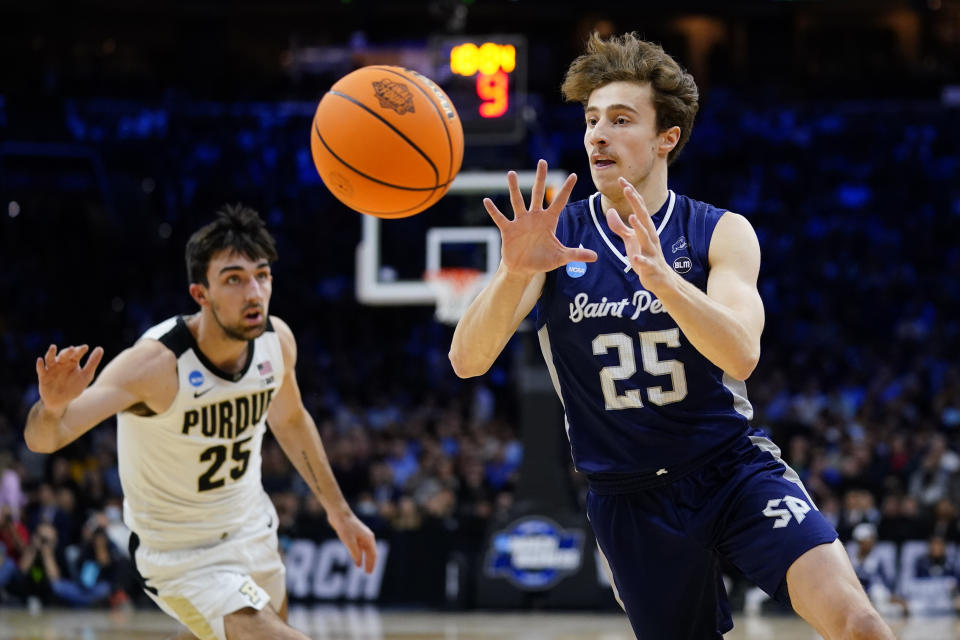 FILE -Saint Peter's Doug Edert, right, reaches for a pass past Purdue's Ethan Morton during the first half of a college basketball game in the Sweet 16 round of the NCAA tournament, Friday, March 25, 2022, in Philadelphia. By the time he and the Peacocks made history by becoming the first 15 seed to advance to the Elite Eight, Edert's mustache had its own Twitter handle and Edert himself had deals hawking chicken wings and a few other products. (AP Photo/Matt Rourke, File)