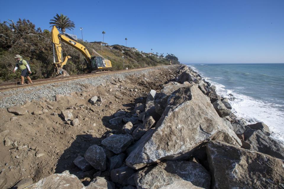 A person and heavy machinery next to big rocks by a coast.