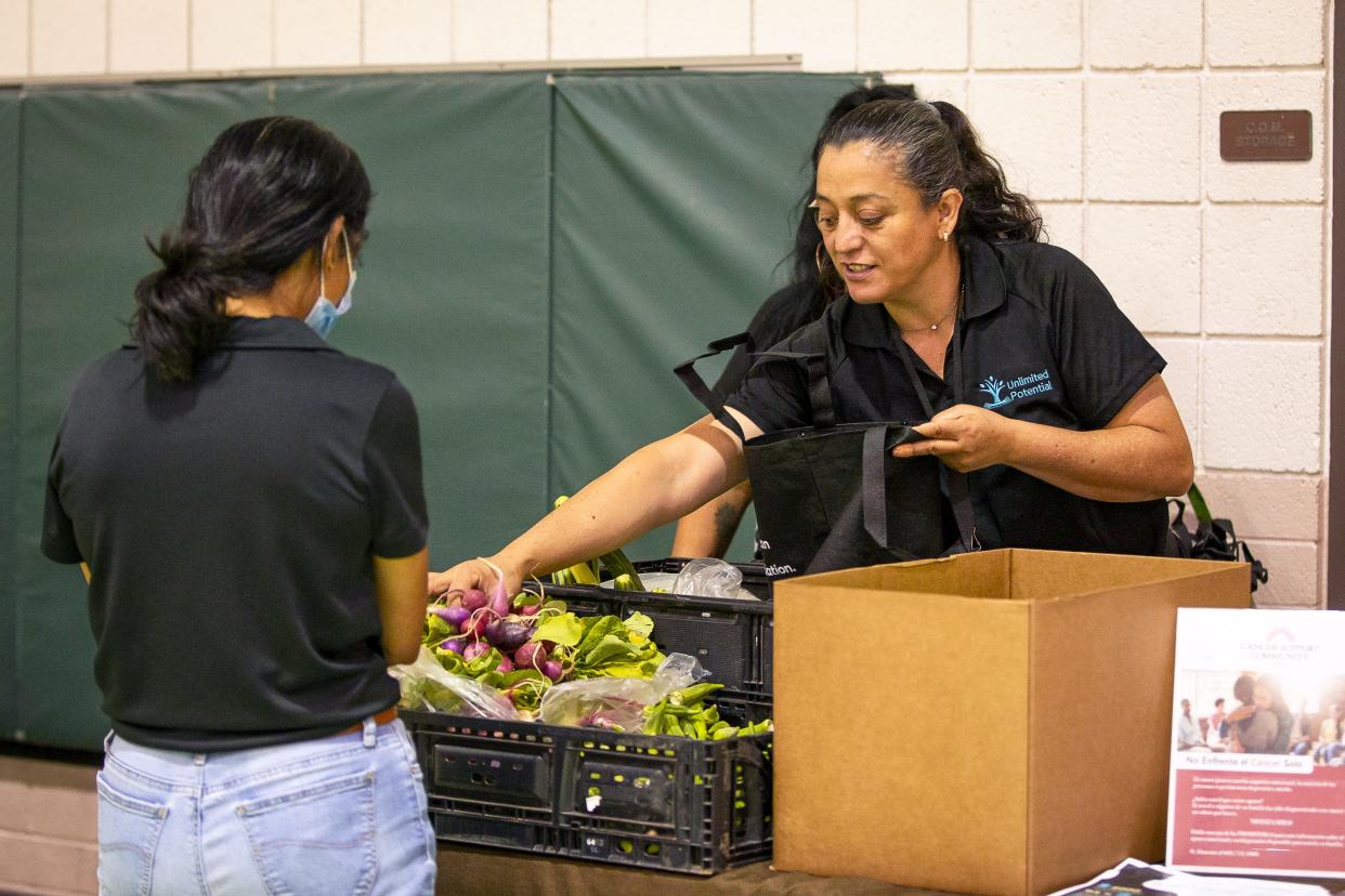 Community health worker Minerva Velarde with Unlimited Potential loads a bag with fresh vegetables for a community member at a health fair event at the Webster Community Center in Mesa on Nov. 2, 2021.