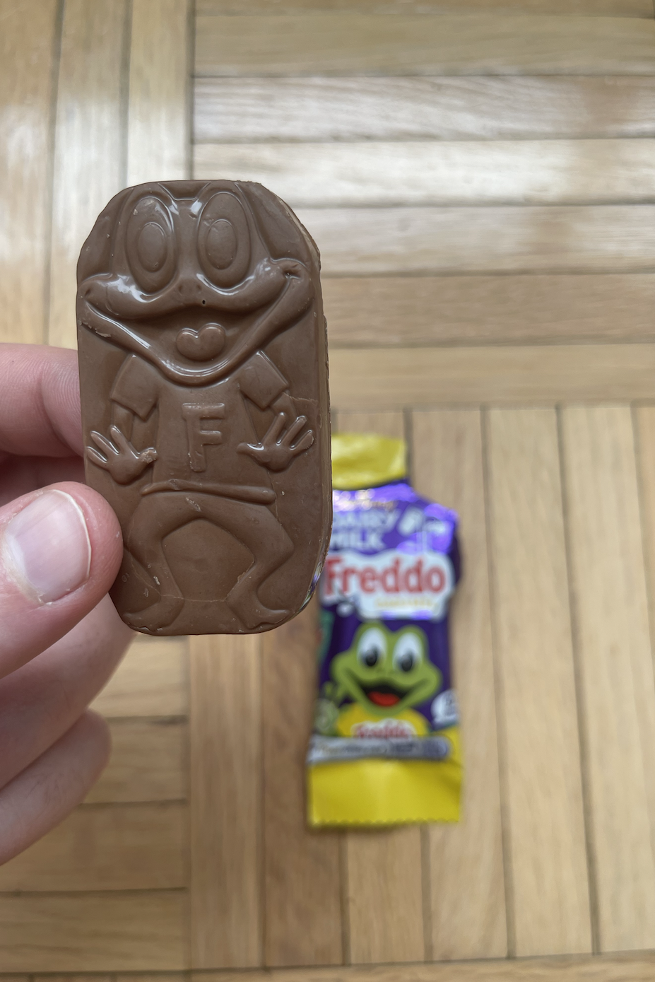 Hand holding a Freddo chocolate bar with another Freddo package in the background