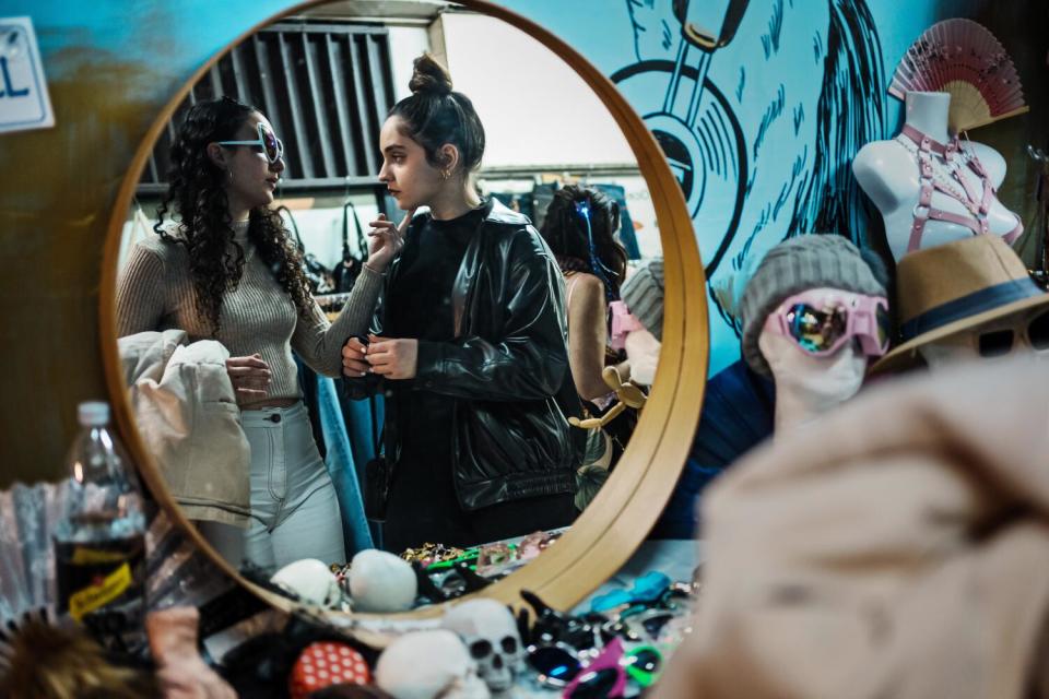 Two teen girls are seen in a round mirror trying on fashion accessories