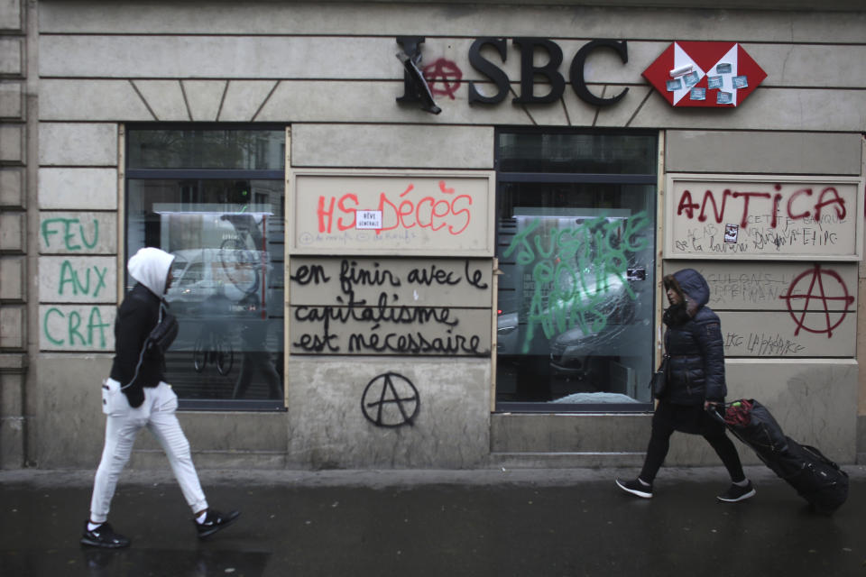 People walk past a vandalized bank after Thursday's violence, Friday, Dec. 6, 2019 in Paris. Frustrated travelers are meeting transportation chaos around France for a second day, as unions dig in for what they hope is a protracted strike against government plans to redesign the national retirement system. (AP Photo/Rafael Yaghobzadeh)