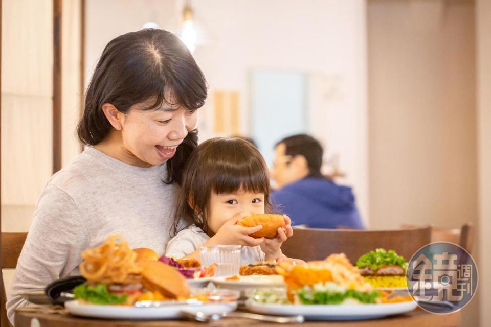 日本小女孩咬一口漢堡笑得好開心。