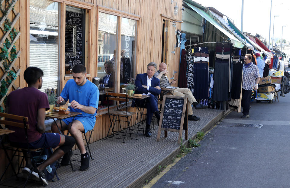 Customers sit in an outdoor coffee shop at Shepherd's bush market that is allowed to reopen after the COVID-19 lockdown in London, Monday, June 1, 2020. The British government has lifted some lockdown restrictions to restart social life and activate the economy while still endeavouring to limit the spread of the highly contagious COVID-19 coronavirus.(AP Photo/Frank Augstein)