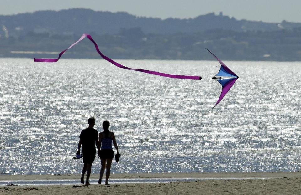 A kite flys past a couple on Crown Memorial Beach Monday, May 12, 2014, in Alameda, Calif. After a hot, windy Mother's Day with temperatures in the mid-80s, a high pressure system was expected to heighten the heat slightly Monday before pushing it to near triple digits in some spots midweek, mostly inland areas already badly parched by drought. High temperatures will extend up and down California, according to the National Weather Service. (AP Photo/Ben Margot)