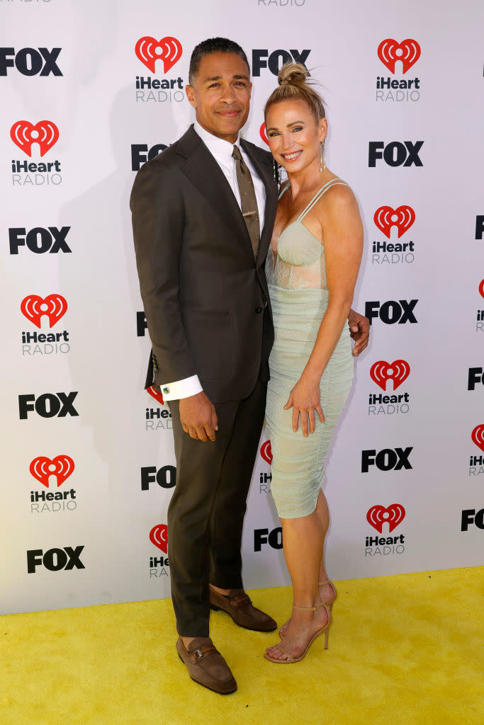 Two individuals posing together at a media event, one in a suit and the other in a sleeveless dress