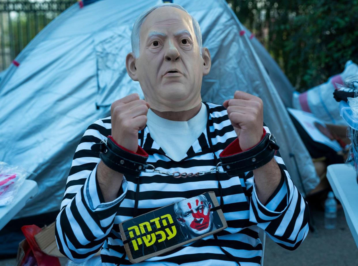 A protestor wears a mask of Israeli Prime Minister Benjamin Netanyahu in handcuffs and prison uniform