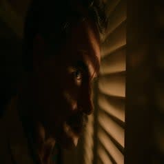 Closeup side view of Armond peering through the slats of a closet, shadows on his face