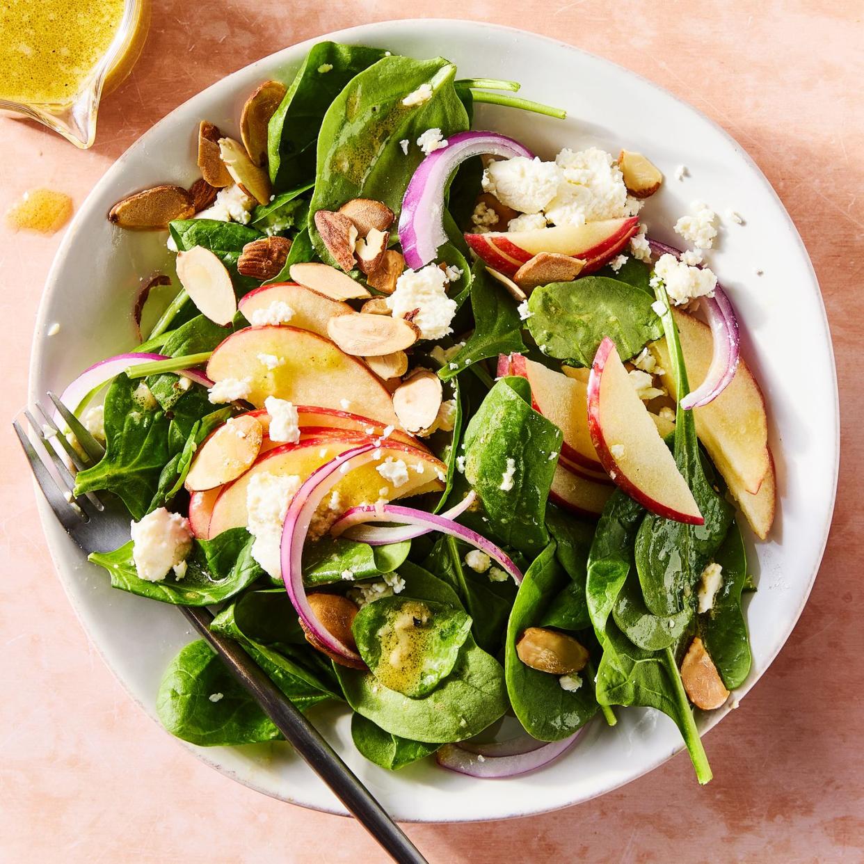 spinach in a bowl topped with sliced apples, sliced almonds, red onions, and crumbled feta