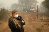 In this Nov. 10, 2018, photo, Arianne Harvey holds her dog T.J. near a truck still on fire from the Camp Fire in Paradise, Calif. Harvey was living in an RV near where her family's home was destroyed by the fire. For a while, Phillip and Krystin Harvey, who lost their mobile home, had been staying with Arianne and their two other teenage daughters in the camper, trying to hang on to a piece of the life they had known. Eventually the family gave up and moved to Oroville, Calif., to stay with friends to have some stability and security, their cousins Patrick Knuthson said. (AP Photo/John Locher)