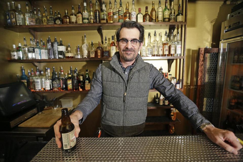 In this April 16, 2014 photo, actor Ty Burrell, who plays bumbling dad Phil Dunphy on ABC's “Modern Family,” poses holding a beer at Bar X, the cocktail bar he co-owns, in Salt Lake City. Burrell just opened Beer Bar, a beer garden-like eatery next door to Bar X that serves 150 beers paired up with an array of house-made bratwursts, local breads and Belgian fries. The restaurant sports long tables and benches with high ceilings to evoke that Bavarian beer hall feel. (AP Photo/Rick Bowmer)