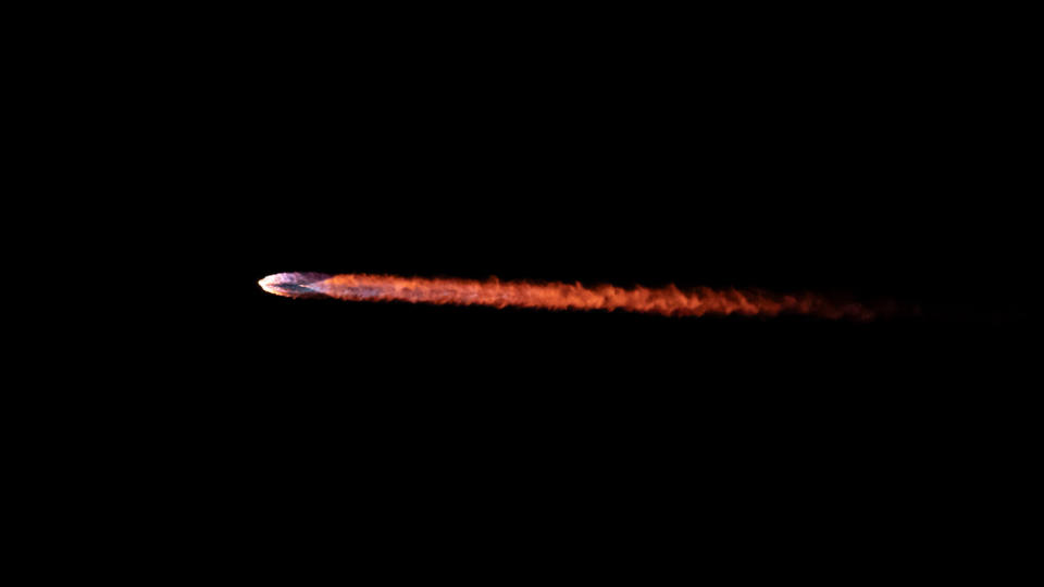 closeup of the trail of flame left by a rocket as it rises into a dark sky