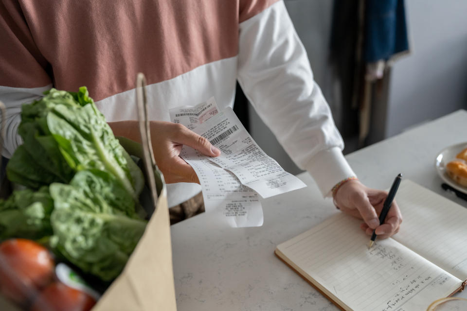 Person budgeting with grocery receipt and notebook, promoting financial wellness