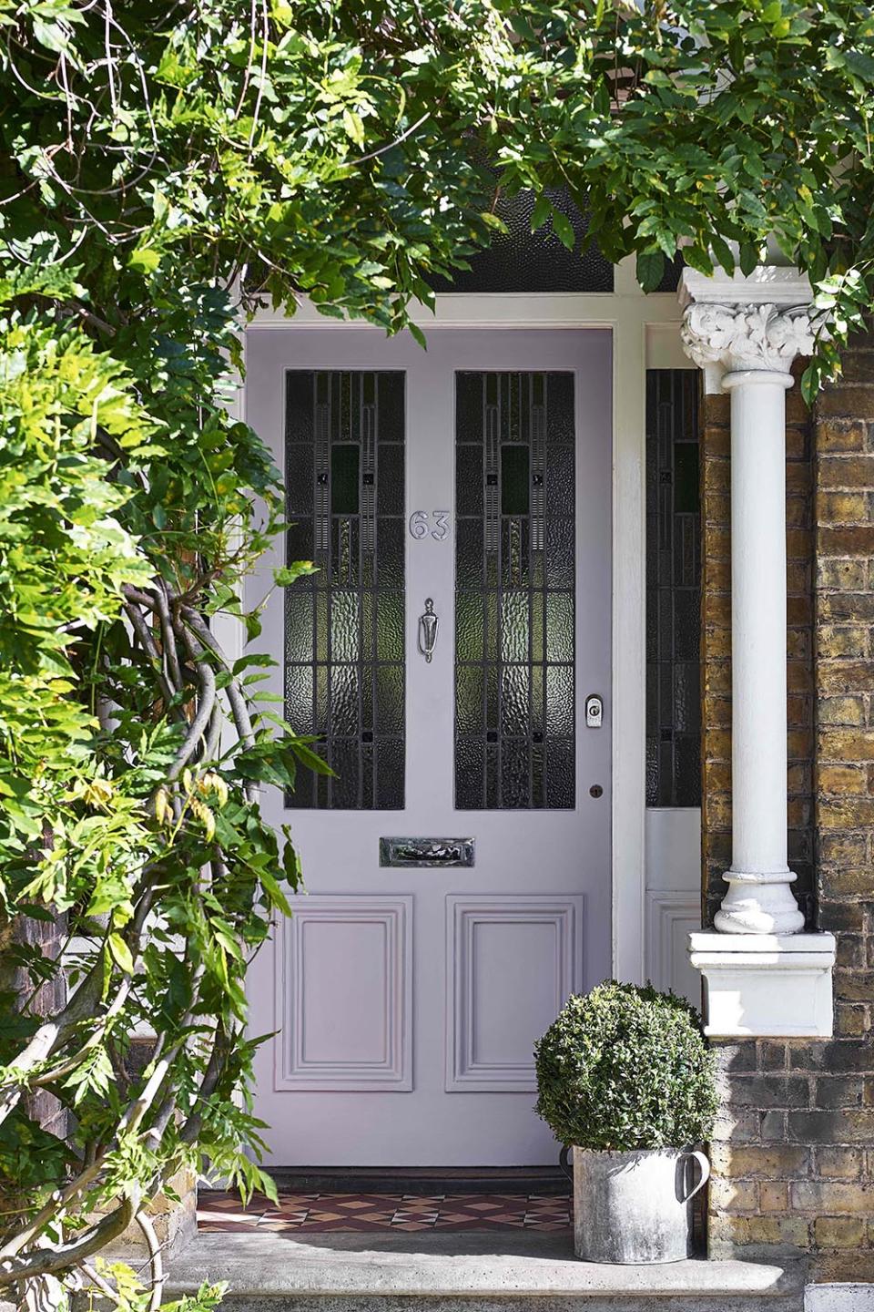 Traditional brick house with pale purple door surrounded by greenery