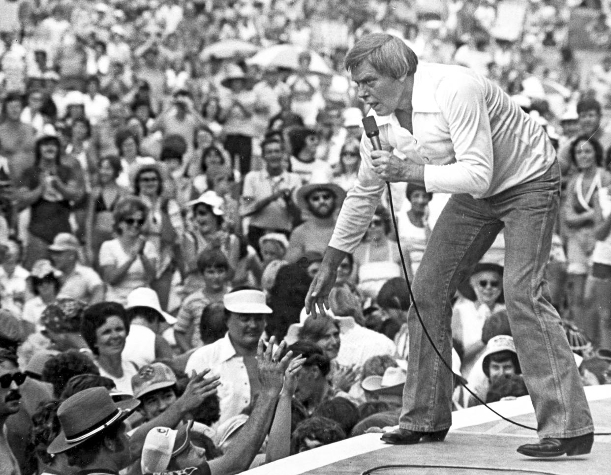 FILE - In this July 16, 1977 file photo, Singer Tom T. Hall leans to the edge of the stage at the Jamboree in the Hills to meet the people near St. Clairsville, Ohio. Singer-songwriter Tom T. Hall, who composed “Harper Valley P.T.A.” and sang about life’s simple joys as country music’s consummate blue collar bard, has died. He was 85. His son, Dean Hall, confirmed the musician's death Friday, Aug. 20, 2021 at his home in Franklin, Tennessee.(AP Photo/File)
