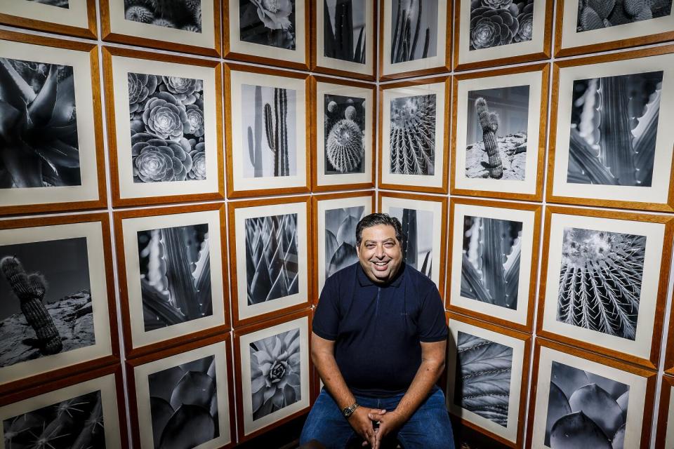 A man sits in a corner surrounded by photos of desert landscapes.
