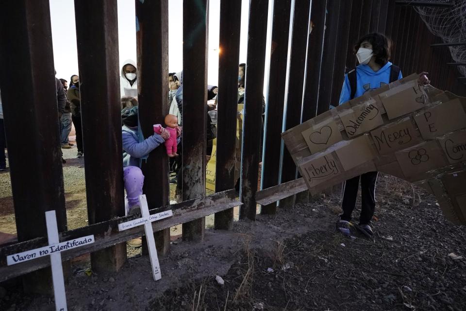 Una niña en México mete su muñeca entre las barreras de la valla fronteriza de Estados Unidos mientras mira a Nathan Adams Maldonado, a la derecha, el martes 15 de diciembre de 2020 durante un evento con varias familias que buscan asilo, en Douglas, Arizona. (AP Foto/Ross D. Franklin)