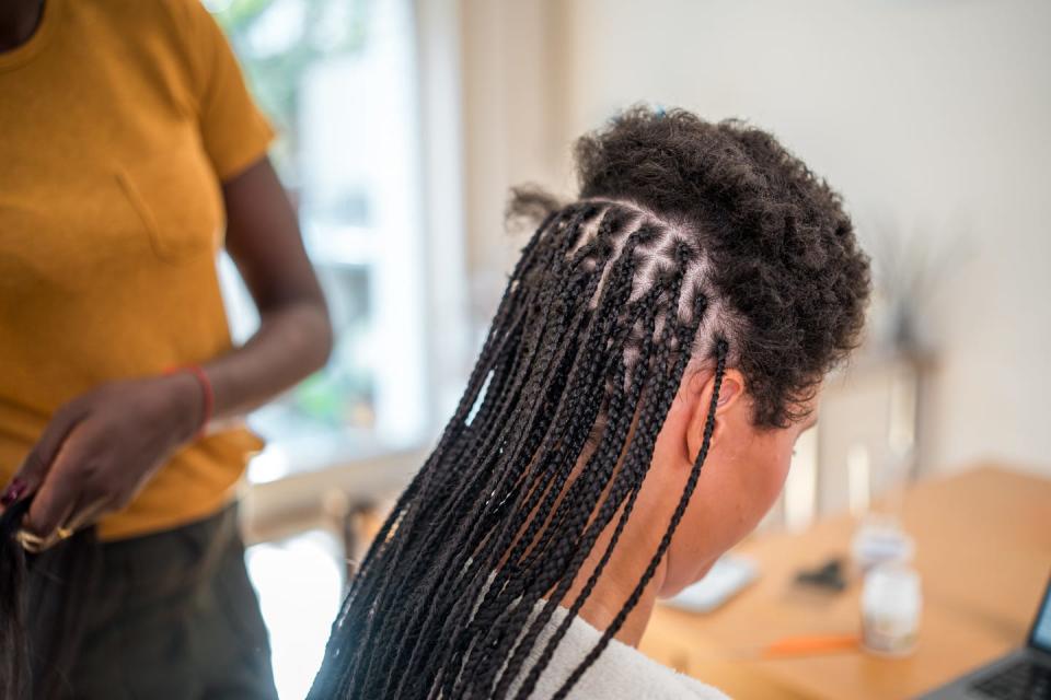 mixed race female having her hair styled into braids by a adult black female in a home setting