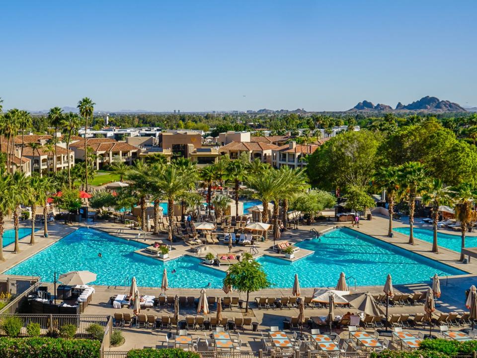 A resort with pools and palm trees in front of a mountain with blue skies in the background