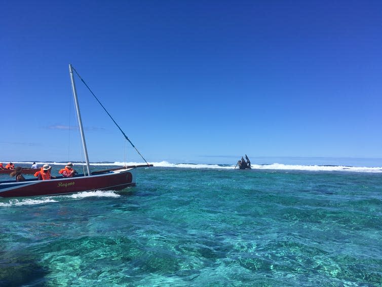 A boat in the coastal lagoon approaches the outer reef where a shipwreck looms.