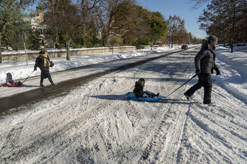 Eric Wettlaufer pulls Grant Wettlaufer, 5, as Natalie Hofert-Wettlaufer pulls Quinn Wettlaufer, 3, on sleds across Forest Avenue in Buffalo, N.Y., Sunday, Nov. 20, 2022. Just south of the city of Buffalo, towns are still working to clear the aftermath of the lake-effect storm. (Libby March/The Buffalo News via AP)