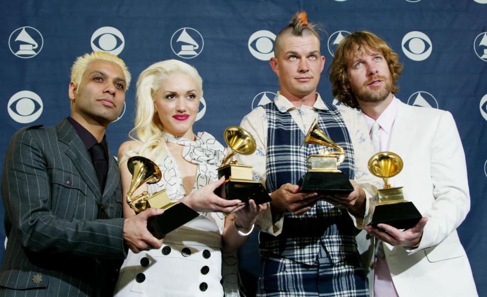 tony kanal, gwen stefani, adrian young, and tom dumont stand in front of a blue background and each hold a grammy trophy